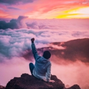 Image of a person sitting on top of a mountain with fist raised in celebration